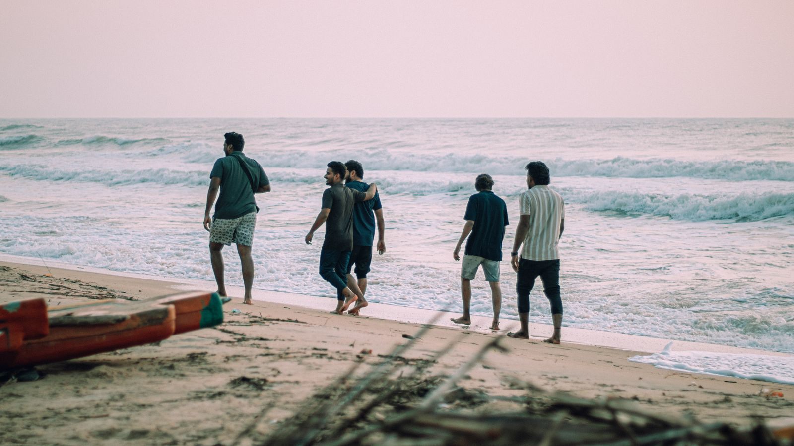 Five friends walking along a beach at sunset