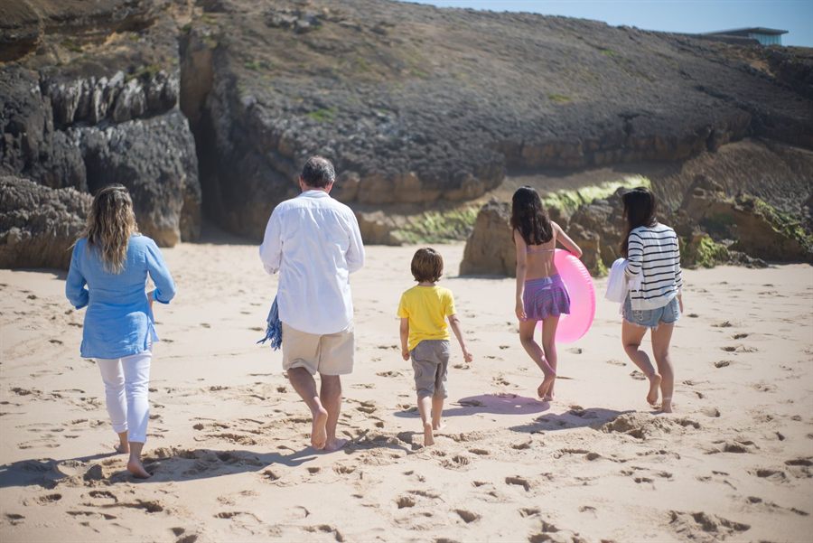 Family walking together across a sunny beach toward the cliffs
