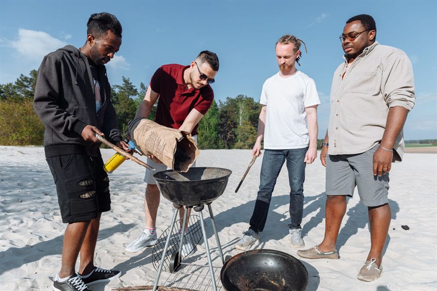 Group of men grilling on a sandy beach on a sunny day
